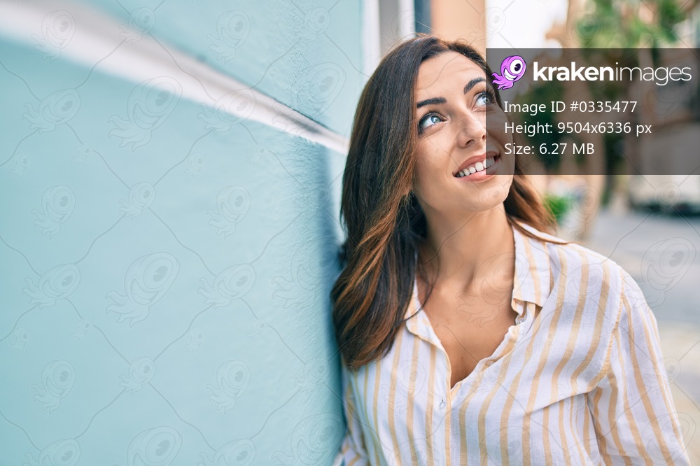 Young hispanic woman smiling happy leaning on the wall at the city.