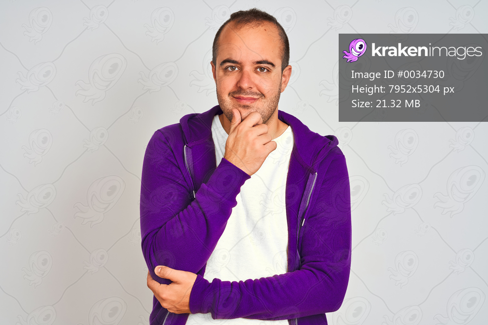 Young man wearing purple sweatshirt standing over isolated white background looking confident at the camera smiling with crossed arms and hand raised on chin. Thinking positive.