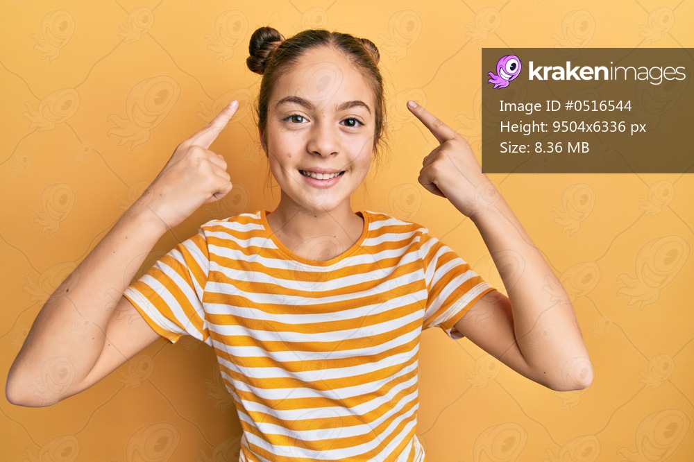 Beautiful brunette little girl wearing casual striped t shirt smiling pointing to head with both hands finger, great idea or thought, good memory 