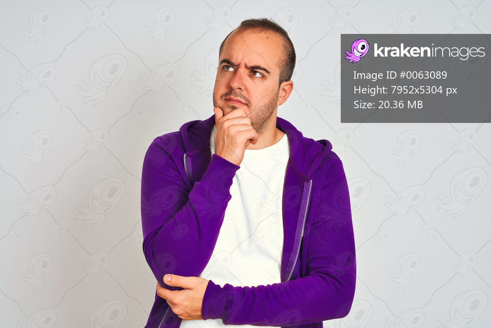 Young man wearing purple sweatshirt standing over isolated white background with hand on chin thinking about question, pensive expression. Smiling with thoughtful face. Doubt concept.