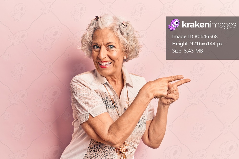 Senior grey-haired woman wearing casual clothes smiling and looking at the camera pointing with two hands and fingers to the side. 