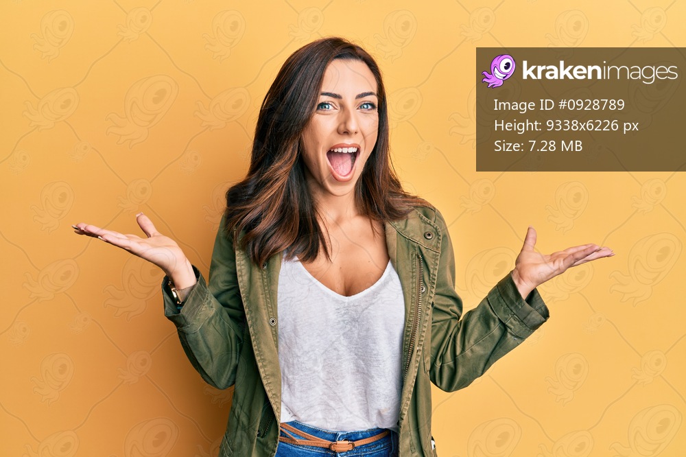 Young brunette woman wearing casual clothes over yellow background celebrating victory with happy smile and winner expression with raised hands 
