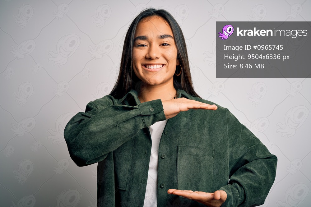Young beautiful asian woman wearing casual shirt standing over isolated white background gesturing with hands showing big and large size sign, measure symbol. Smiling looking at the camera. Measuring concept.