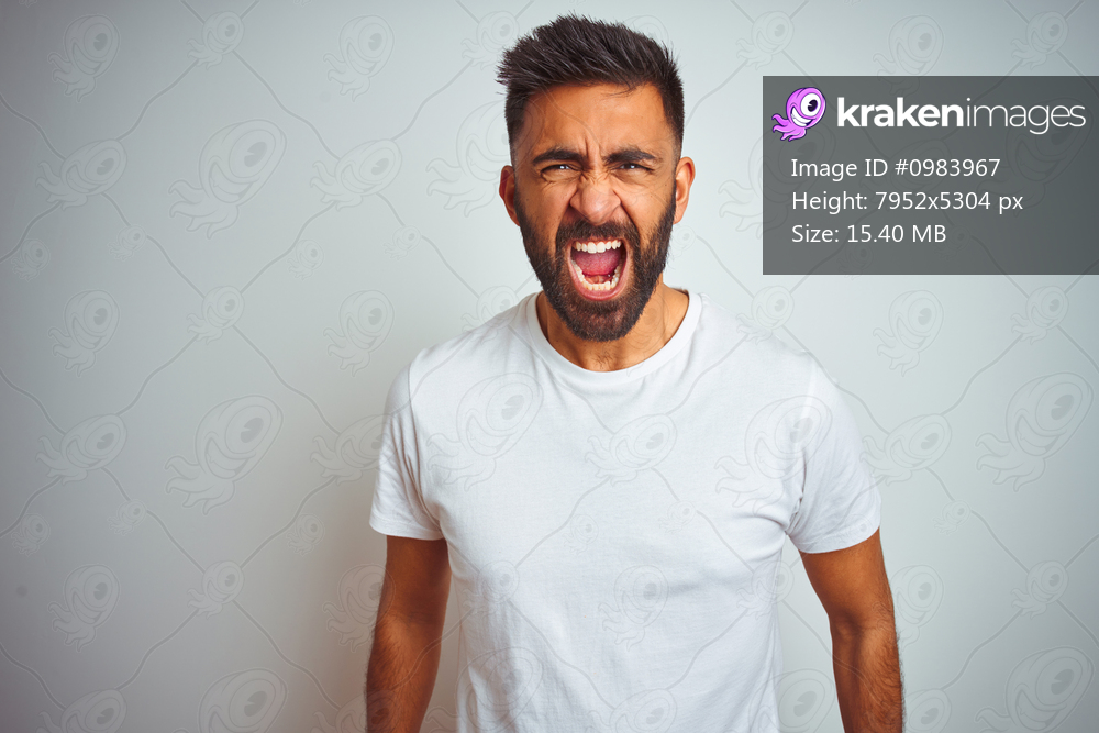 Young indian man wearing t-shirt standing over isolated white background angry and mad screaming frustrated and furious, shouting with anger. Rage and aggressive concept.