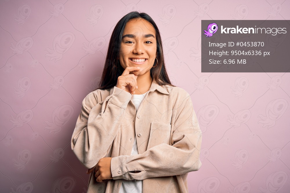 Young beautiful asian woman wearing casual shirt standing over pink background looking confident at the camera smiling with crossed arms and hand raised on chin. Thinking positive.