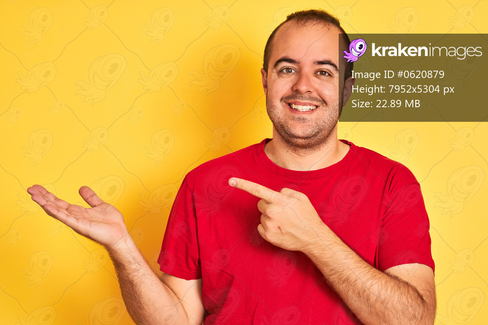 Young man wearing red casual t-shirt standing over isolated yellow background very happy pointing with hand and finger