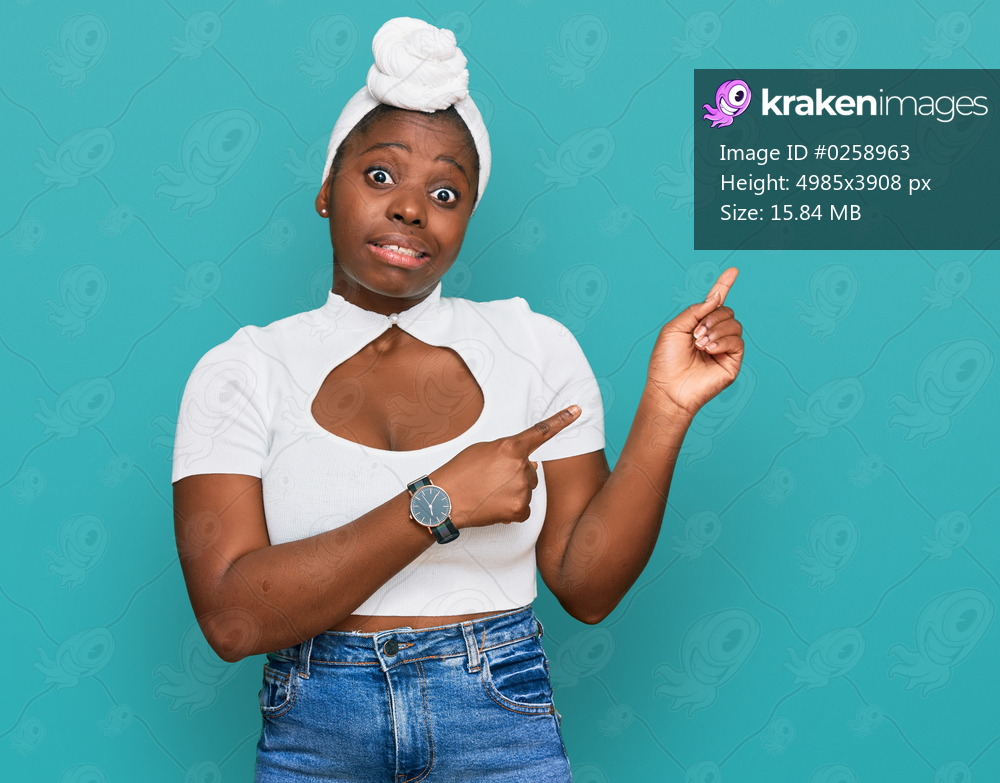 Young african woman with turban wearing hair turban over isolated background pointing aside worried and nervous with both hands, concerned and surprised expression 