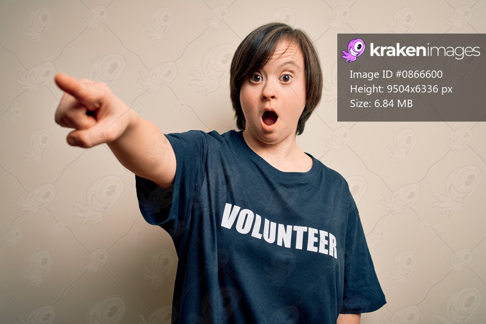 Young down syndrome volunteer woman wearing social care charity t-shirt Pointing with finger surprised ahead, open mouth amazed expression, something on the front