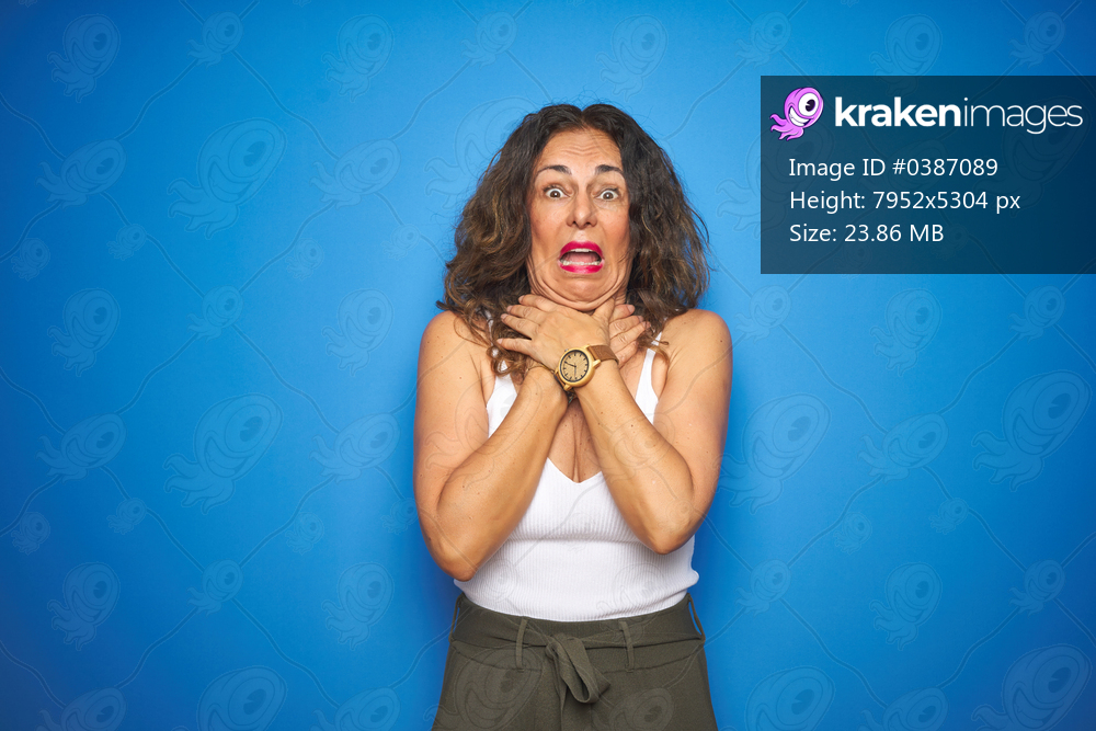 Middle age senior woman with curly hair standing over blue isolated background shouting suffocate because painful strangle. Health problem. Asphyxiate and suicide concept.