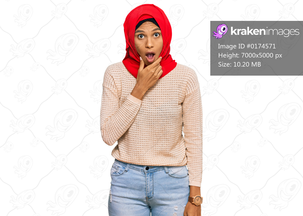Young african american woman wearing traditional islamic hijab scarf looking fascinated with disbelief, surprise and amazed expression with hands on chin 