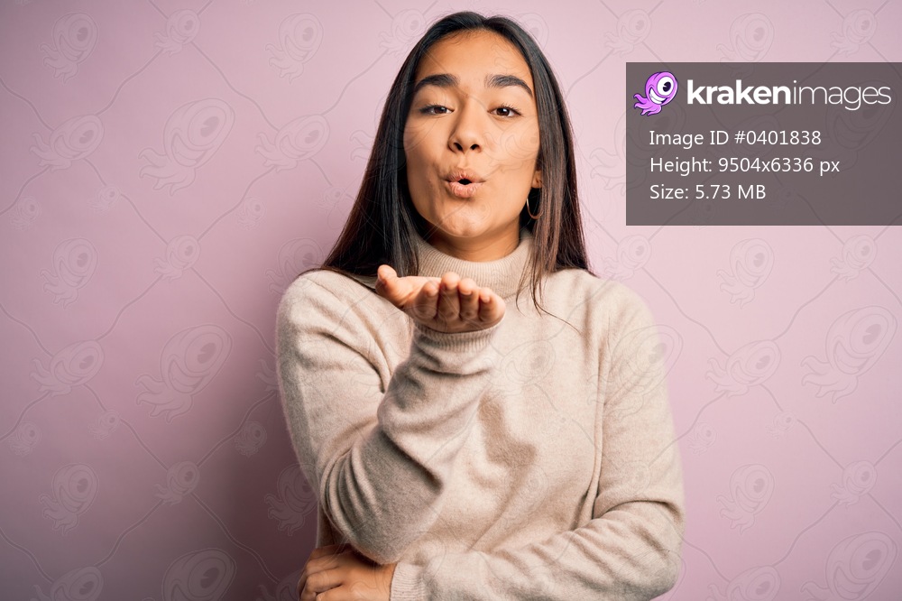 Young beautiful asian woman wearing casual turtleneck sweater over pink background looking at the camera blowing a kiss with hand on air being lovely and sexy. Love expression.