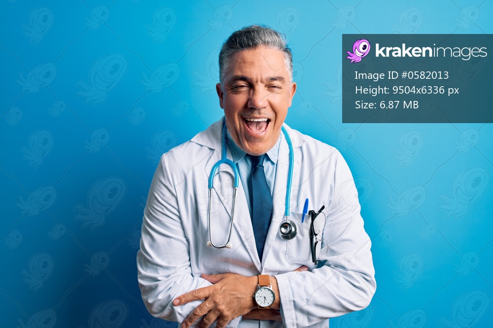 Middle age handsome grey-haired doctor man wearing coat and blue stethoscope smiling and laughing hard out loud because funny crazy joke with hands on body.