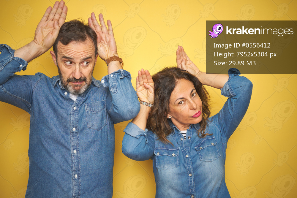 Beautiful middle age couple together standing over isolated yellow background Doing bunny ears gesture with hands palms looking cynical and skeptical. Easter rabbit concept.
