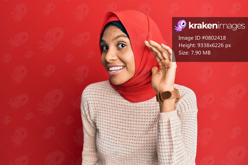 Young african american woman wearing traditional islamic hijab scarf smiling with hand over ear listening and hearing to rumor or gossip. deafness concept. 