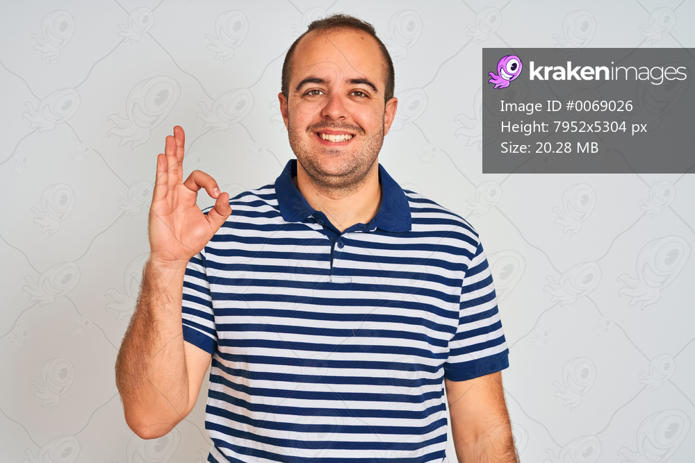 Young man wearing casual striped polo standing over isolated white background smiling positive doing ok sign with hand and fingers. Successful expression.