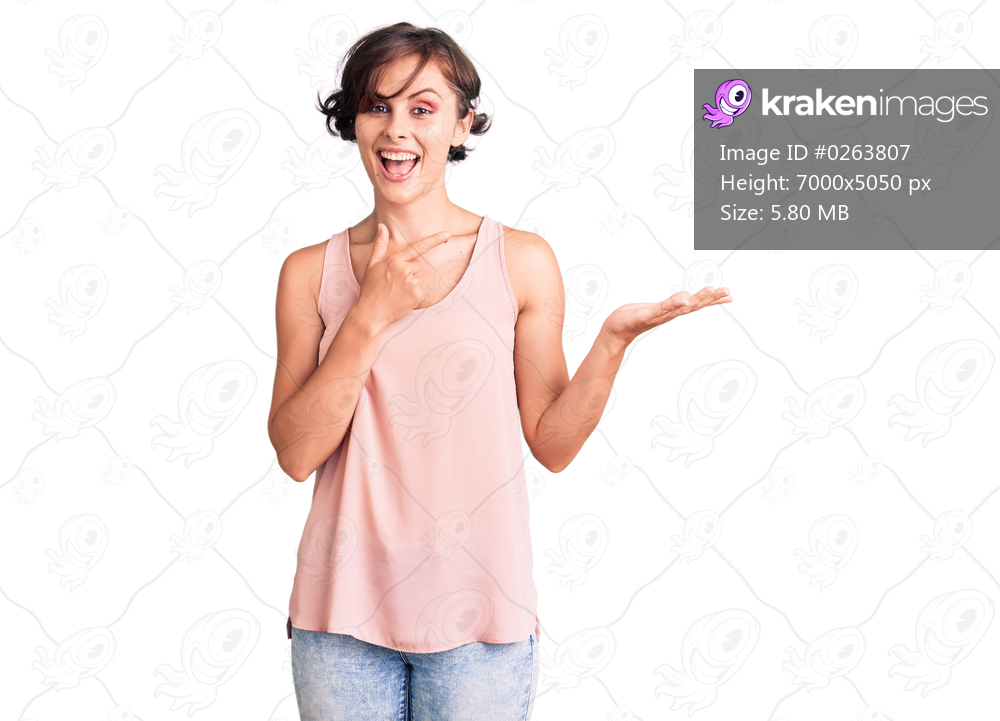 Beautiful young woman with short hair wearing casual style with sleeveless shirt amazed and smiling to the camera while presenting with hand and pointing with finger. 