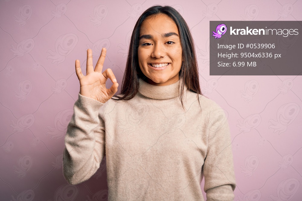Young beautiful asian woman wearing casual turtleneck sweater over pink background smiling positive doing ok sign with hand and fingers. Successful expression.