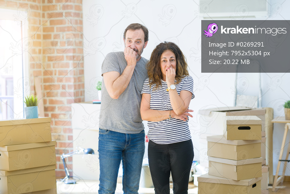 Middle age senior couple moving to a new home with boxes around looking stressed and nervous with hands on mouth biting nails. Anxiety problem.