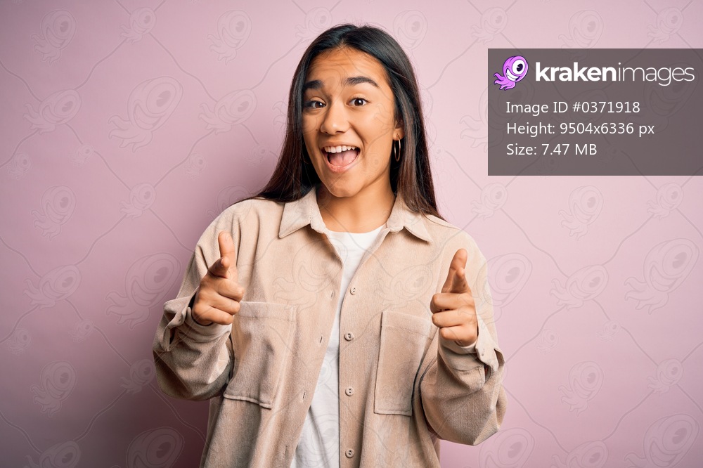 Young beautiful asian woman wearing casual shirt standing over pink background pointing fingers to camera with happy and funny face. Good energy and vibes.
