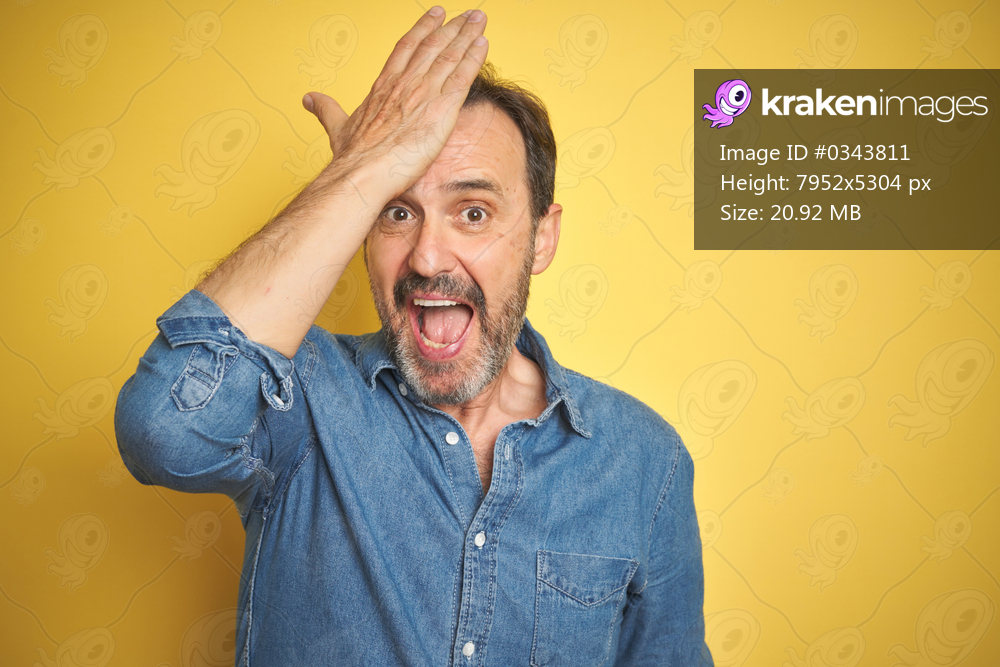 Handsome middle age senior man with grey hair over isolated yellow background surprised with hand on head for mistake, remember error. Forgot, bad memory concept.
