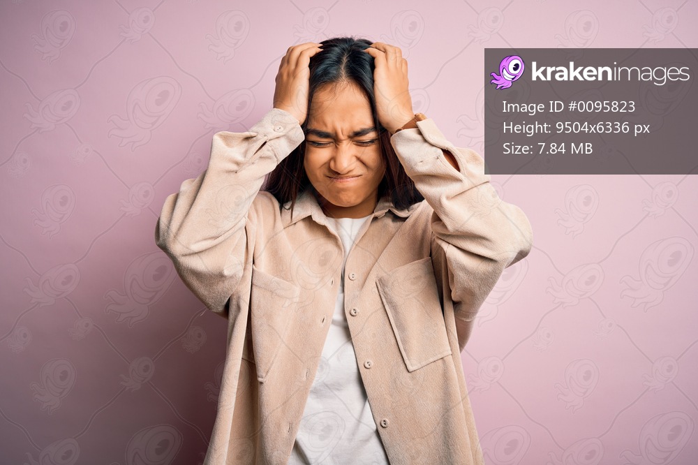 Young beautiful asian woman wearing casual shirt standing over pink background suffering from headache desperate and stressed because pain and migraine. Hands on head.