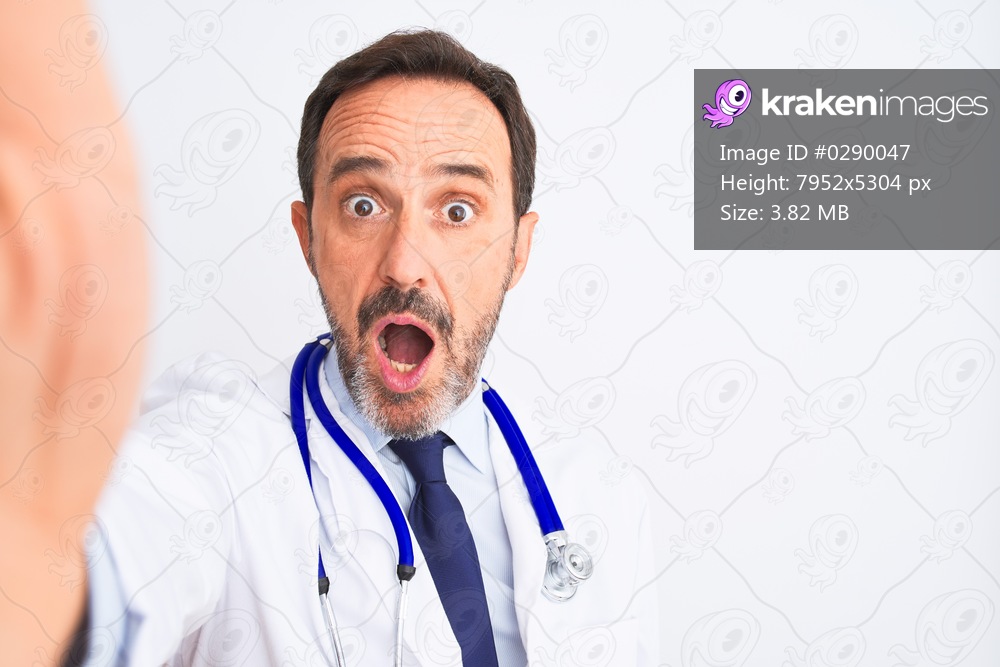 Middle age doctor man wearing stethoscope make selfie over isolated white background scared in shock with a surprise face, afraid and excited with fear expression