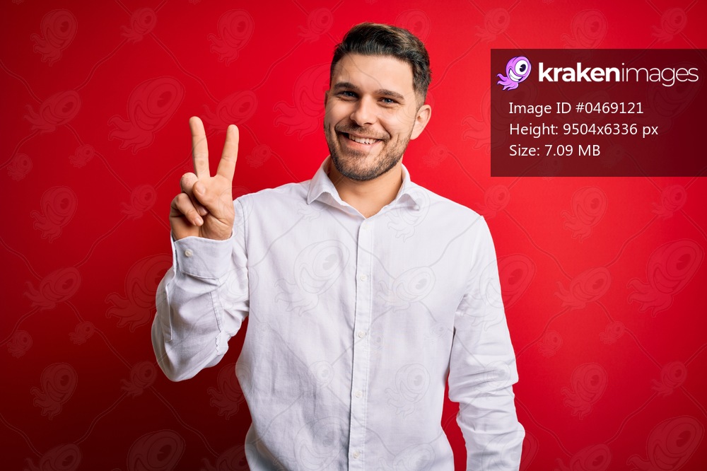 Young business man with blue eyes wearing elegant shirt standing over red isolated background showing and pointing up with fingers number two while smiling confident and happy.