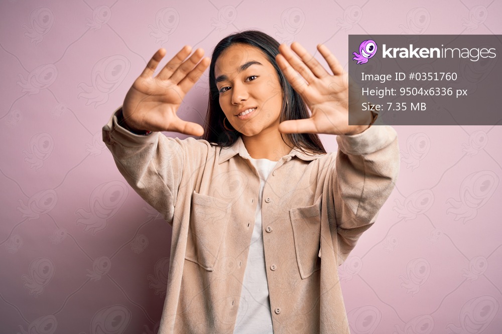 Young beautiful asian woman wearing casual shirt standing over pink background doing frame using hands palms and fingers, camera perspective