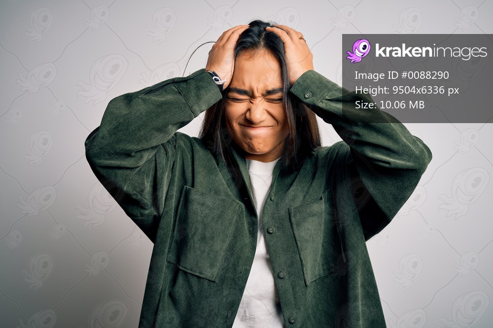 Young beautiful asian woman wearing casual shirt standing over isolated white background suffering from headache desperate and stressed because pain and migraine. Hands on head.