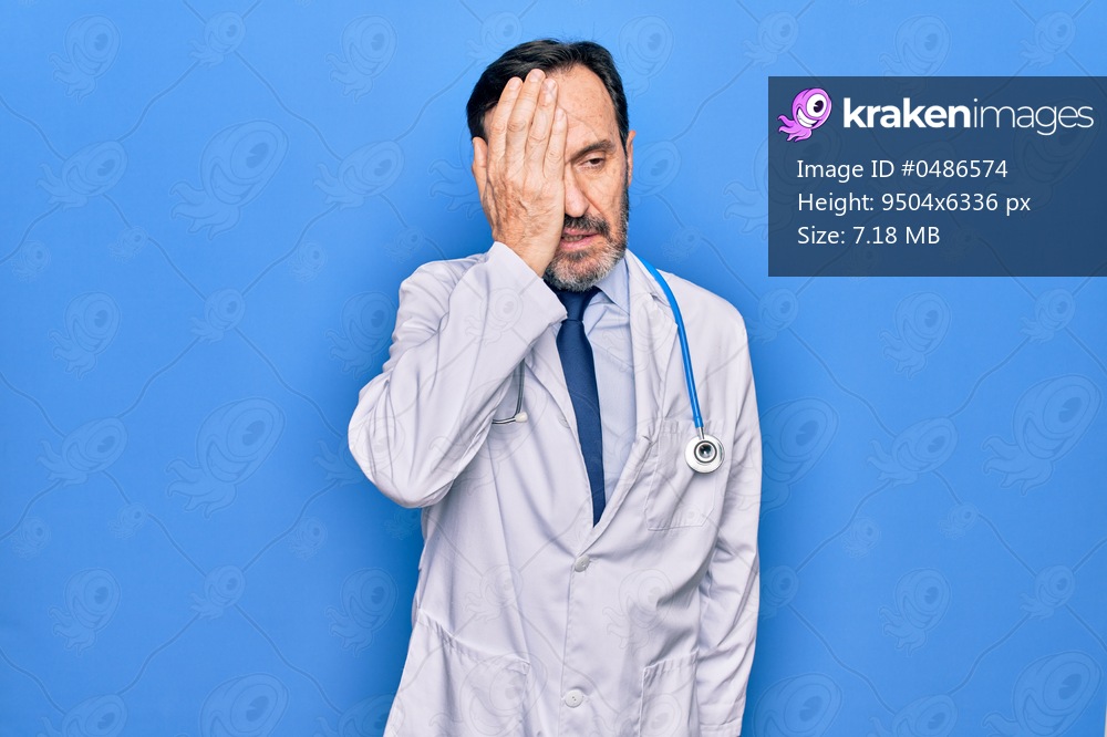Middle age handsome doctor man wearing coat and stethoscope over isolated blue background surprised with hand on head for mistake, remember error. Forgot, bad memory concept.
