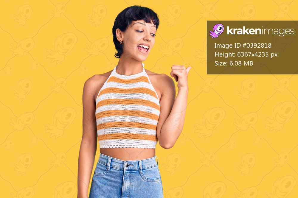 Young brunette woman with short hair wearing casual clothes smiling with happy face looking and pointing to the side with thumb up. 