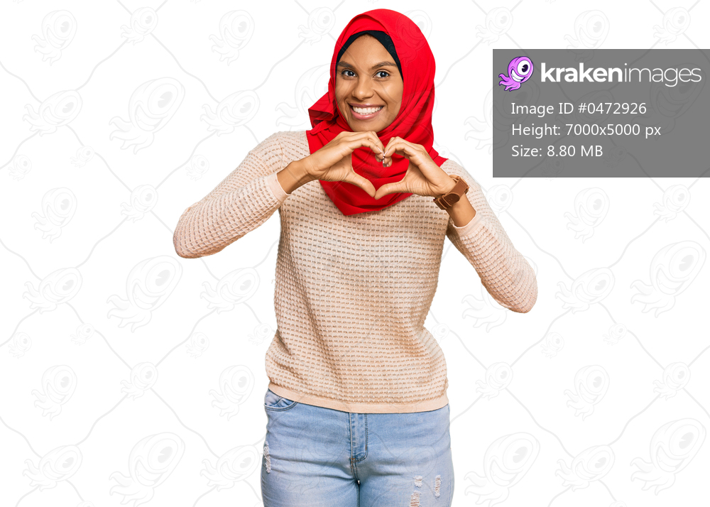 Young african american woman wearing traditional islamic hijab scarf smiling in love doing heart symbol shape with hands. romantic concept. 