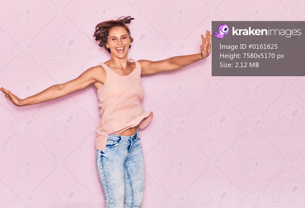Young beautiful woman wearing casual clothes smiling happy. Jumping with smile on face and arms opened over isolated pink background.