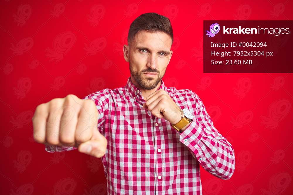 Young handsome man over red isolated background Punching fist to fight, aggressive and angry attack, threat and violence