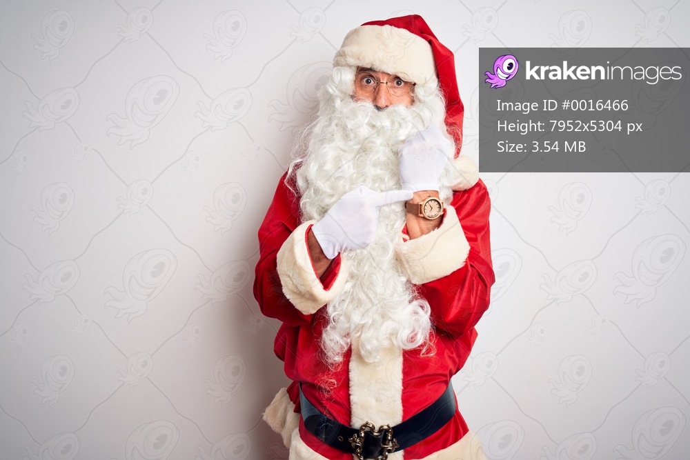 Middle age handsome man wearing Santa costume standing over isolated white background In hurry pointing to watch time, impatience, looking at the camera with relaxed expression