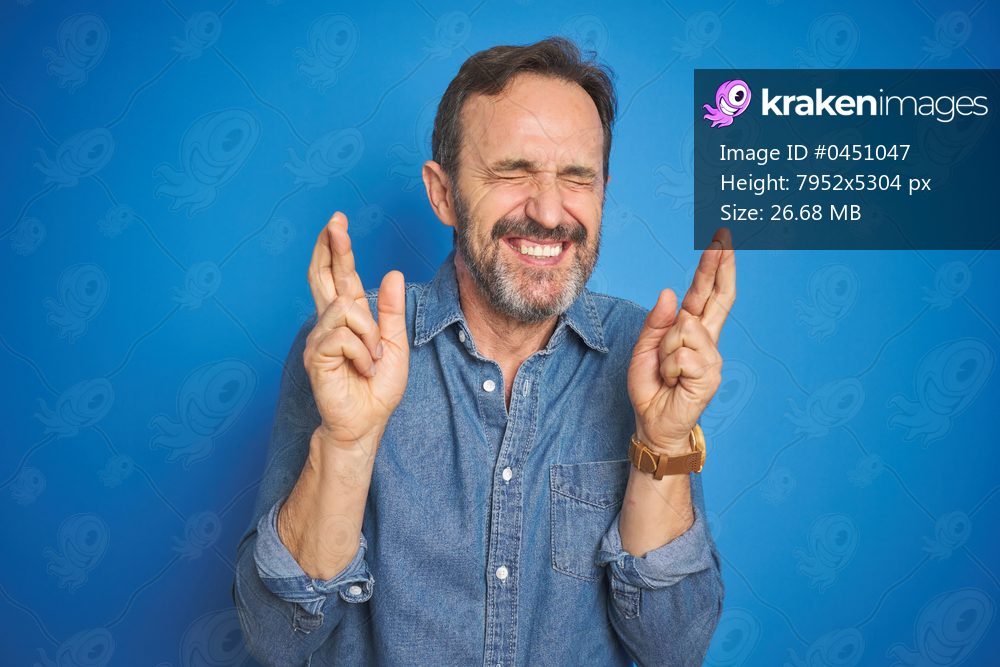 Handsome middle age senior man with grey hair over isolated blue background gesturing finger crossed smiling with hope and eyes closed. Luck and superstitious concept.