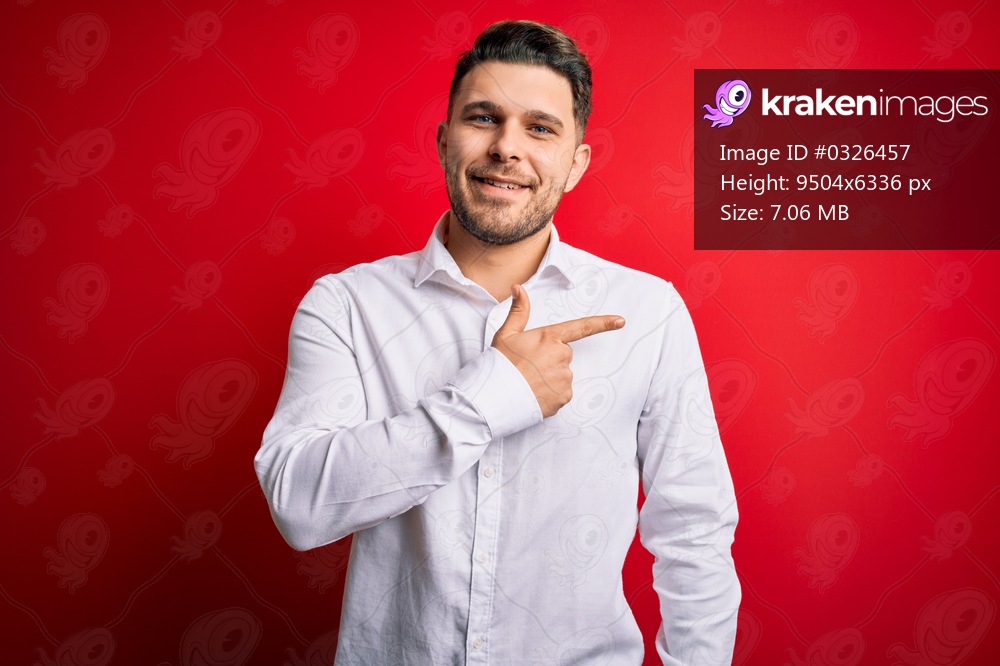 Young business man with blue eyes wearing elegant shirt standing over red isolated background cheerful with a smile on face pointing with hand and finger up to the side with happy and natural expression