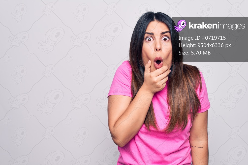 Young beautiful brunette woman wearing casual pink t-shirt standing over white background Looking fascinated with disbelief, surprise and amazed expression with hands on chin
