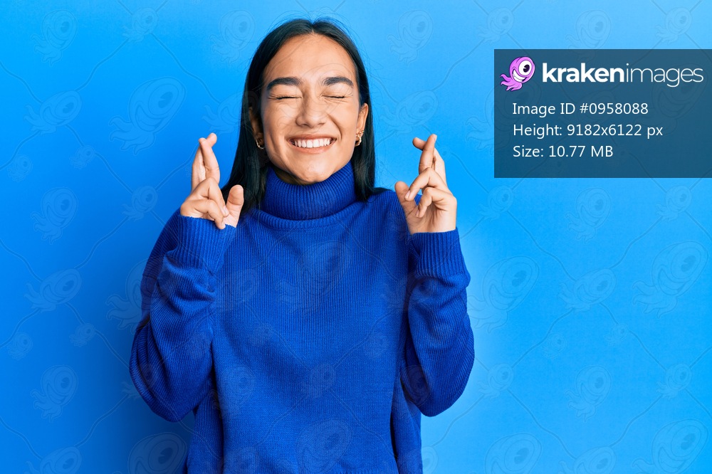 Young asian woman wearing casual winter sweater gesturing finger crossed smiling with hope and eyes closed. luck and superstitious concept. 