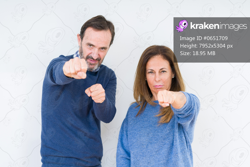 Beautiful middle age couple in love over isolated background Punching fist to fight, aggressive and angry attack, threat and violence