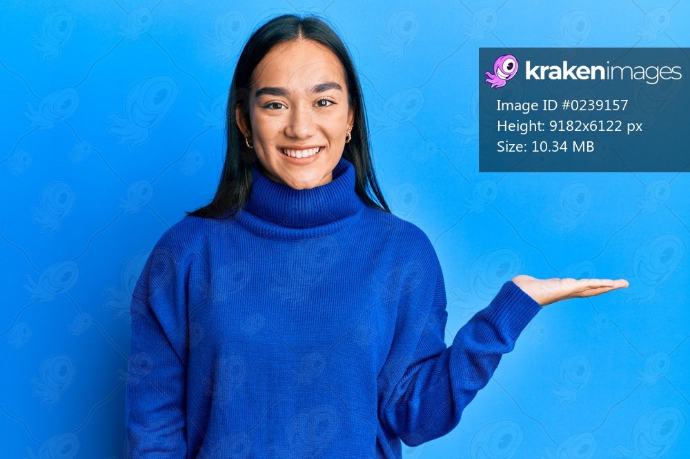 Young asian woman wearing casual winter sweater smiling cheerful presenting and pointing with palm of hand looking at the camera. 