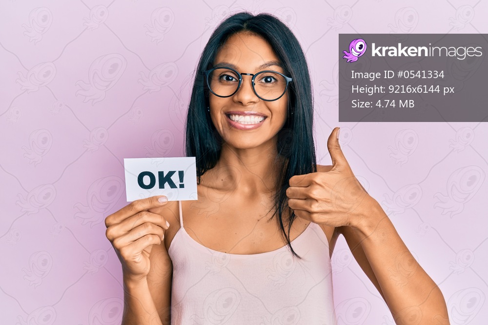 Young african american woman holding ok message paper smiling happy and positive, thumb up doing excellent and approval sign 