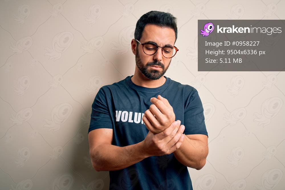 Handsome man with beard wearing t-shirt with volunteer message over white background Suffering pain on hands and fingers, arthritis inflammation