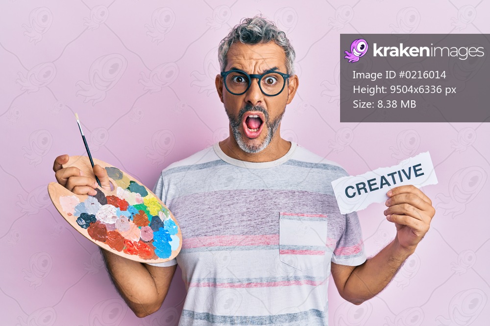 Middle age grey-haired man holding palette and creative message paper afraid and shocked with surprise and amazed expression, fear and excited face. 