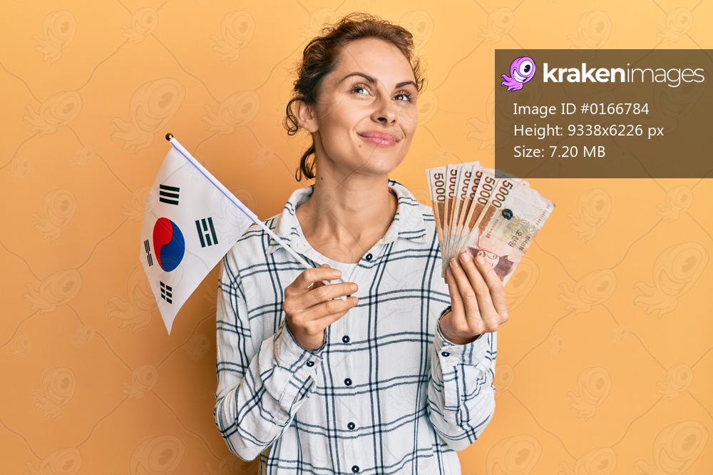 Young brunette woman holding south korean won banknotes smiling looking to the side and staring away thinking. 