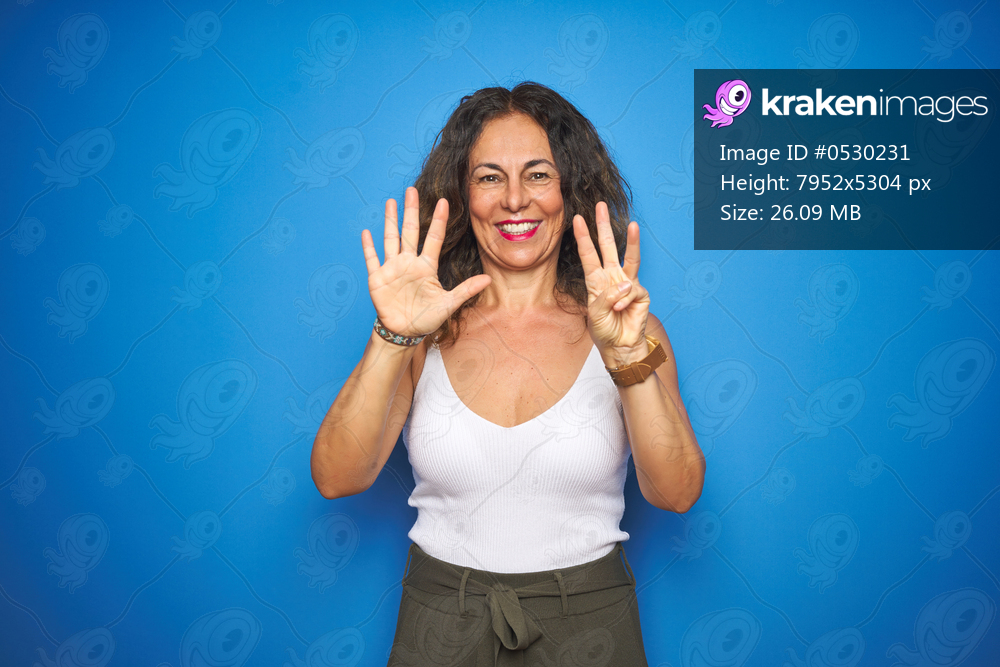 Middle age senior woman with curly hair standing over blue isolated background showing and pointing up with fingers number eight while smiling confident and happy.