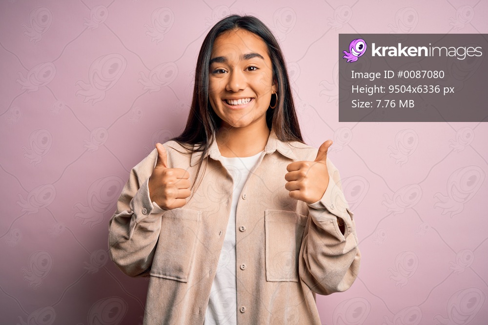 Young beautiful asian woman wearing casual shirt standing over pink background success sign doing positive gesture with hand, thumbs up smiling and happy. Cheerful expression and winner gesture.