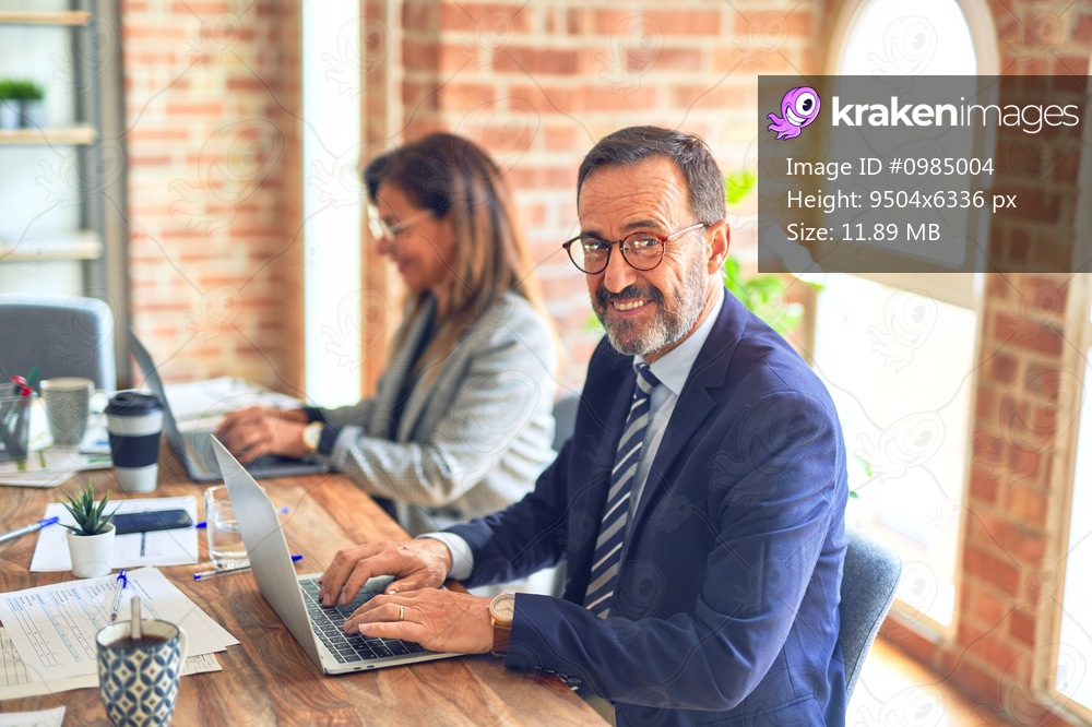 Two middle age business workers smiling happy and confident. Working together with smile on face using laptop at the office