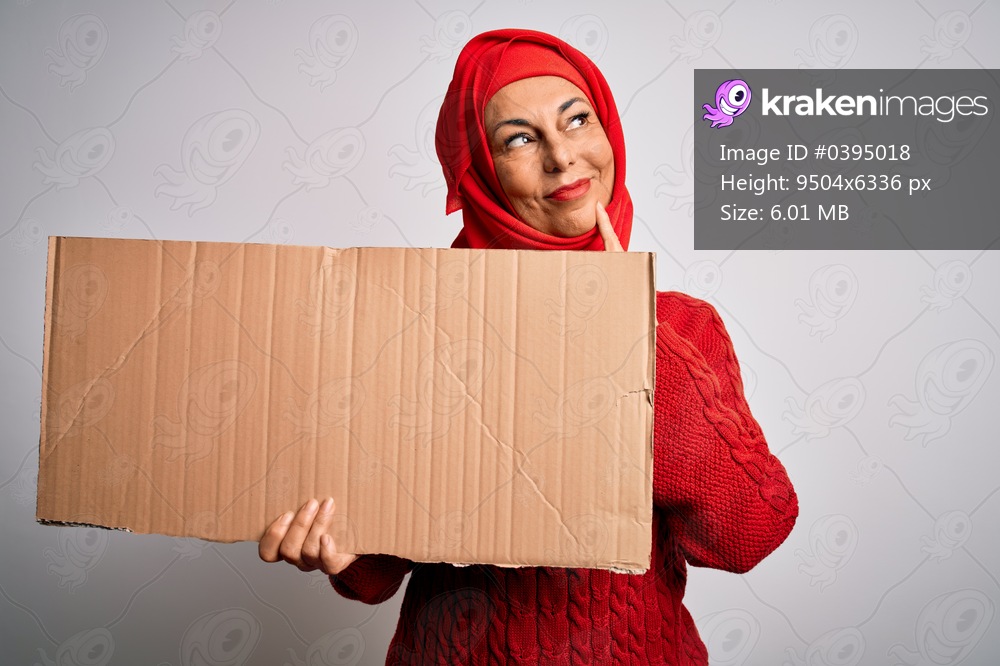 Middle age brunette woman wearing traditional muslim hijab holding banner serious face thinking about question, very confused idea
