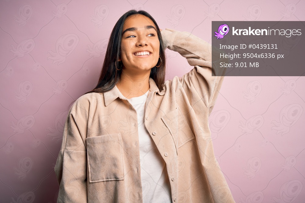 Young beautiful asian woman wearing casual shirt standing over pink background smiling confident touching hair with hand up gesture, posing attractive and fashionable